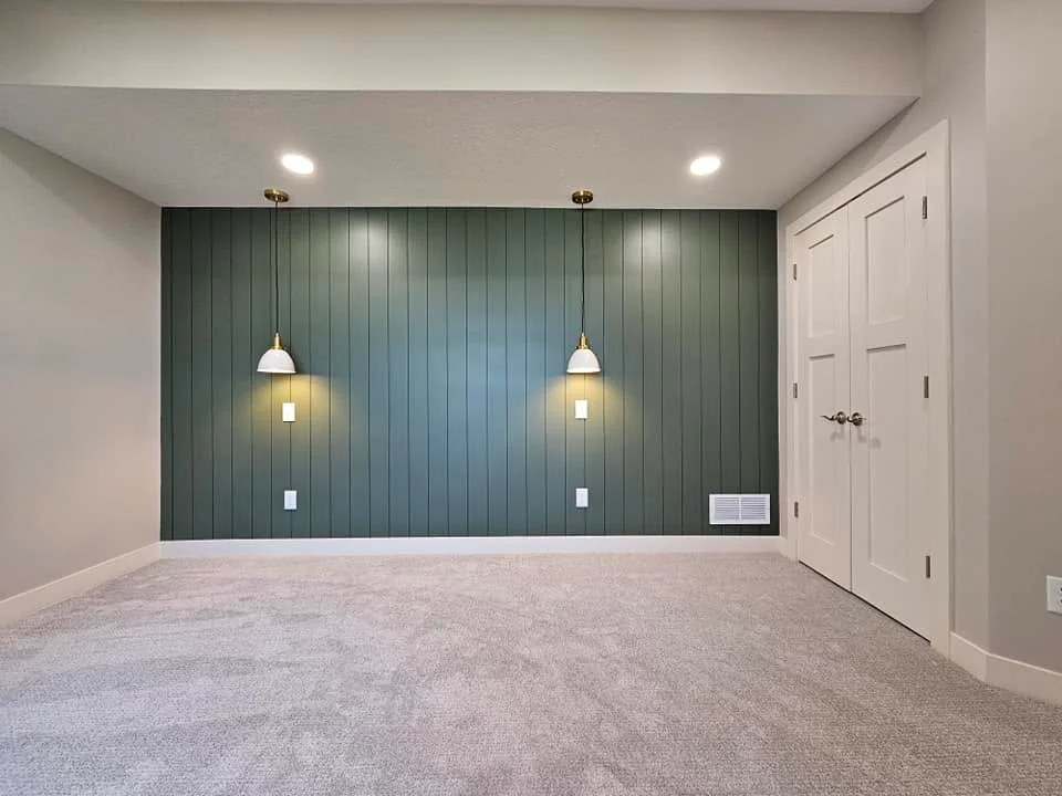 Finished basement room with dark green vertical shiplap accent wall, pendant lights, and new carpet flooring