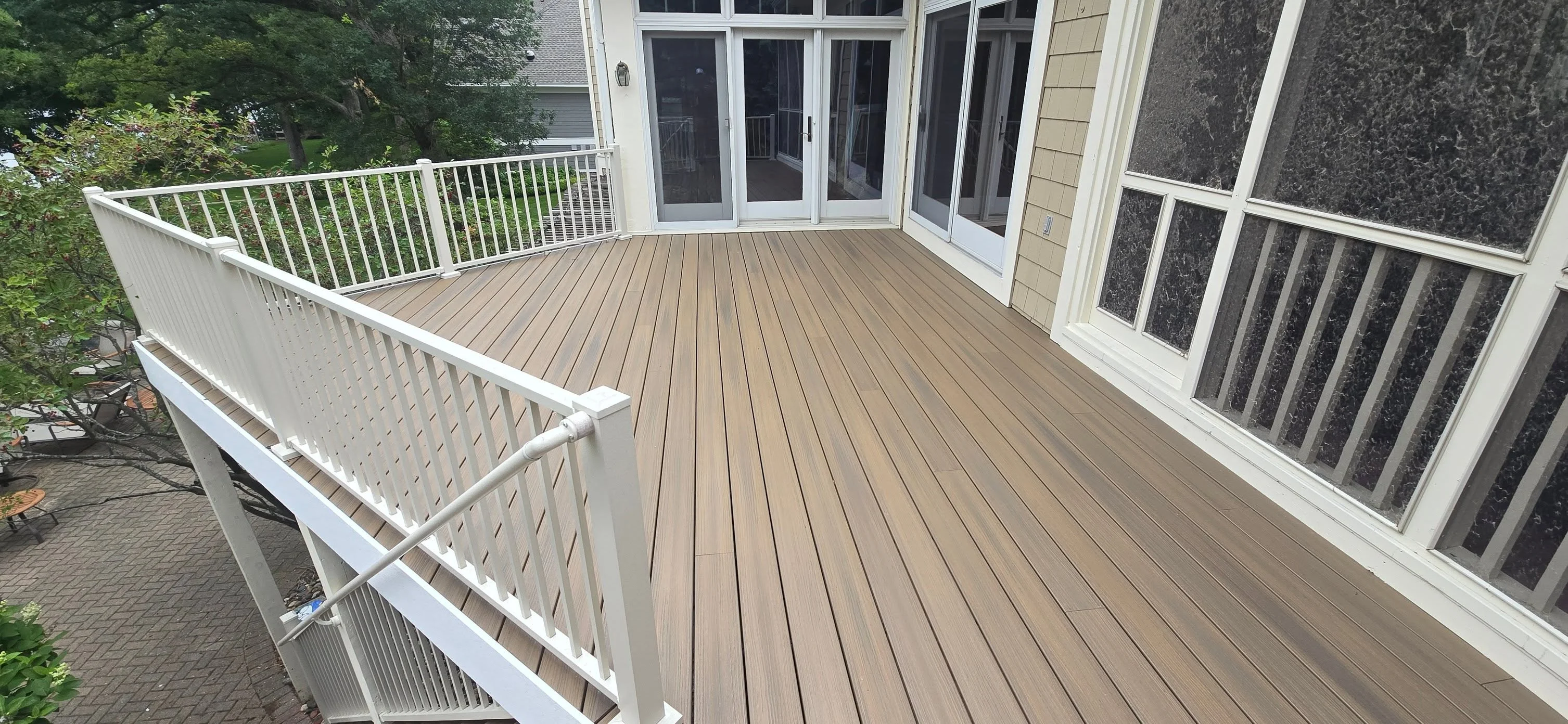 Large composite deck with white railings and balusters attached to home with French doors